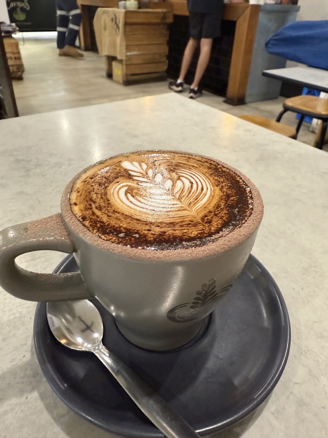 Cappuccino dusted with cocoa and finished with fern latte art on a marble bench